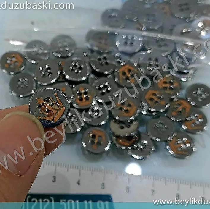 Metal düğme üzerine baskı, lazer ile metal düğmeye baskı, nikelajlı metal düğme üzerine kazıma ve altta bakır alanın çıkarılması işlemidir, adetli lazer baskı, markalama